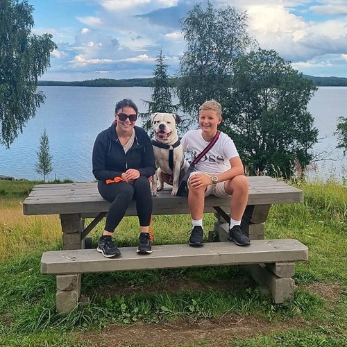 Erika med son och hund i somrigt landskap med sjö i bakgrunden.