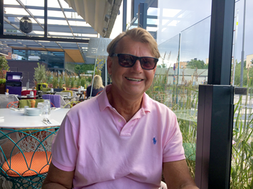 Ingvar har på sig rosa poloskjorta och glasögon. Han ler mot kameran. I bakgrunden skymtar en restaurang.